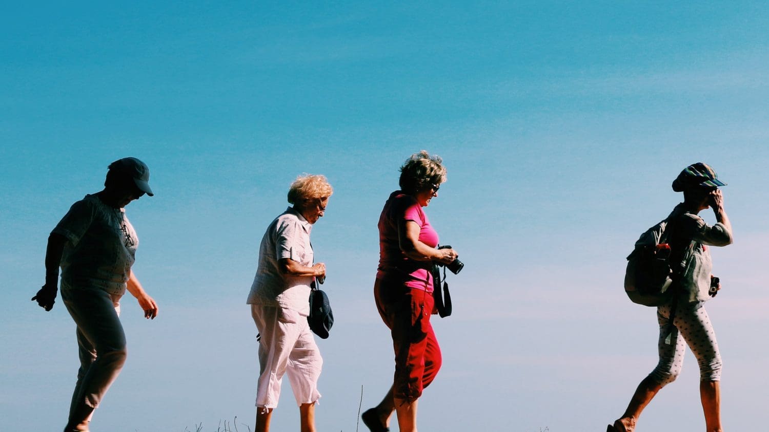4 women in hiking wear walking with a blue sky background